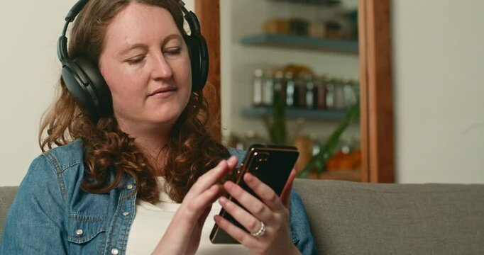 Pregnant Woman Relaxing on Sofa, Listening to Music on Smartphone with Headphones