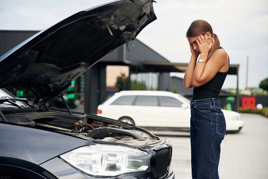 Hood is opened, shocked person. Woman's car is broken, accident, standing outdoors