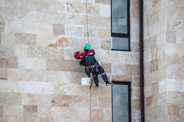 A man is hanging from a building with a bucket in his hand