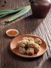 A plate of steamed Indonesian siomay served with a side of dipping sauce. Fresh green onions and a traditional teapot are placed nearby on a rustic wooden table, creating a simple yet inviting scene.