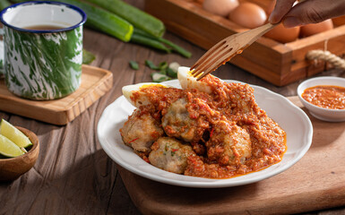 A plate of traditional siomai, a type of Indonesian steamed dumpling served with a spicy peanut sauce and accompanied by hard-boiled eggs. a hand holding a fork is lifting a piece
