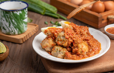 A plate of traditional siomai, a type of Indonesian steamed dumpling served with a spicy peanut sauce and accompanied by hard-boiled eggs. a hand holding a fork is lifting a piece