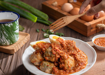 A plate of traditional siomai, a type of Indonesian steamed dumpling served with a spicy peanut sauce and accompanied by hard-boiled eggs. a hand holding a fork is lifting a piece