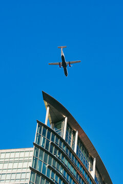 An airplane gracefully flies over a uniquely styled modern building against a clear blue sky, capturing the intersection of travel, technology, and innovative urban design in London UK