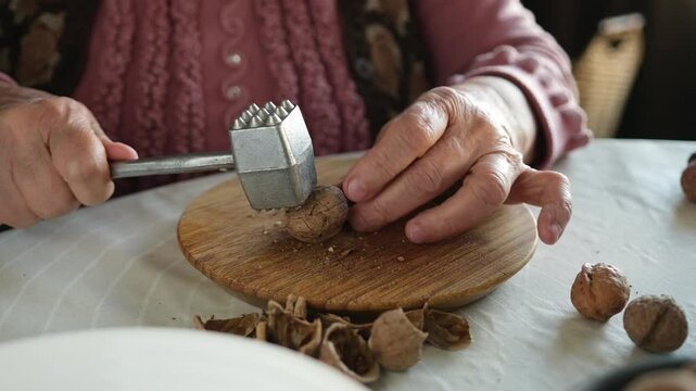 An elderly woman breaks the hard shells of walnuts with an iron hammer.