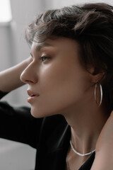Fototapeta premium The woman gently touches her hair, revealing her graceful profile. The soft afternoon light illuminates her features in a minimalistic indoor setting, creating a calm and reflective atmosphere