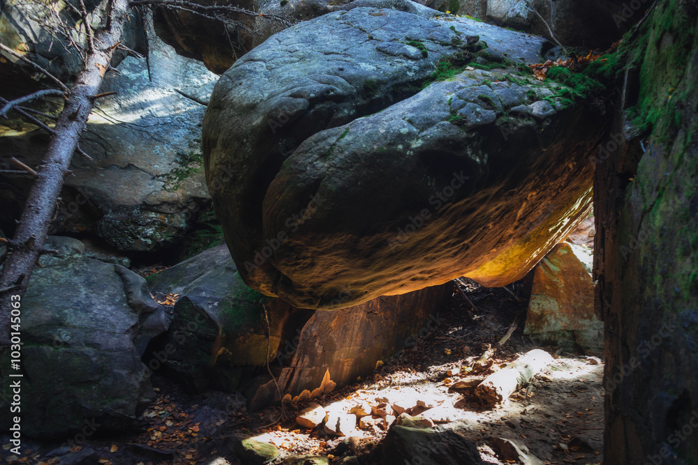 Poster afternoon sun illuminates a gigantic boulder precariously balanced between two stone formations in a