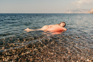 A woman is floating on a pink inflatable raft in the ocean. The water is calm and the sky is clear. The woman is enjoying her time in the water.