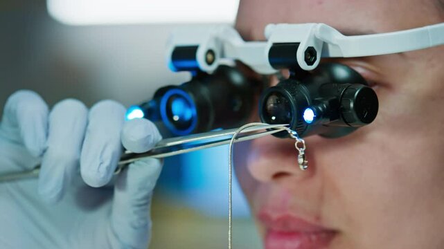 Close up view of female forensic scientist of jeweller in gloves examining silver chain with magnifying glasses in laboratory