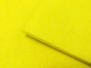a close-up of a bright yellow surface, which appears to be a piece of fabric or a similar material. There is a visible edge or fold in the fabric, creating a slight shadow and giving the image some