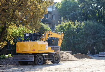 A large yellow tractor hauls sand and building materials to the site. People build a house, a playground or a parking lot for cars on the street. Construction of a new facility in the park.