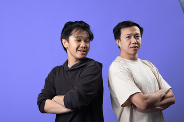 Two Asian men stand side by side with their arms crossed, smiling confidently against a purple background. One wears a black hoodie, and the other a white T-shirt with a bear illustration