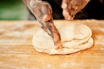 Person, hands and kneading with dough for pastry, bread or production on wooden table at bakery. Closeup, baker or chef with flour, ingredients or wheat for handmade rolls, food or heast on desk