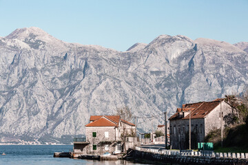Fototapeta premium Bay of Kotor, Montenegro. Stone houses by the waterfront with red-tiled roofs, set against a backdrop of rugged mountains