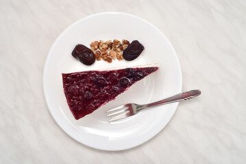 Piece of homemade cheesecake, broken walnut kernels, fresh dates and small dessert fork on the white plate. Top view. 
