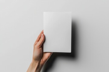 Fototapeta premium A close-up of a hand holding a blank white vertikal flyer, isolated on a white background. Perfect for mockups, branding, and advertising concepts.
