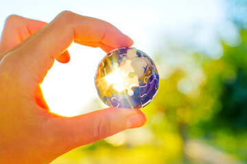 Hand Holding Globe Puzzle with Sun Rays Coming Through the Missing Pieces