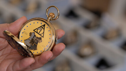 Fototapeta premium Budokan Geek Convention In GUAYAQUIL, ECUADOR - OCT 13, 2024 - Close-up of a hand holding a golden pocket watch with a Harry Potter-inspired design featuring the Deathly Hallows symbol.
