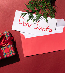 Christmas composition with tartan pattern gift box and Dear Santa concept letter on the red background. Winter holiday greeting card.