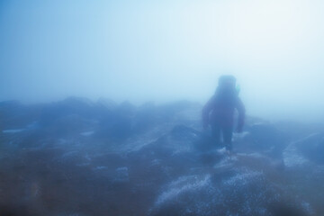 At the edge of the world. Silhouette of hiker on top of a mountain in fog and clouds in the...