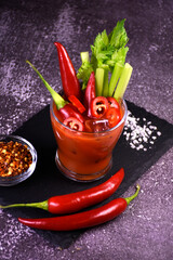 Bloody Mary alcoholic cocktail decorated with hot pepper and celery on a dark background. Serving a drink at the bar.