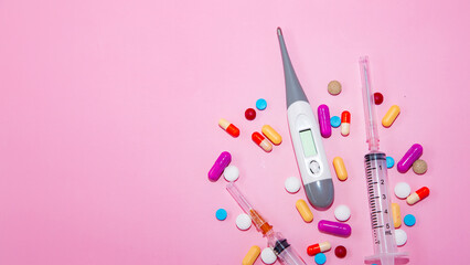 Colorful pills and capsules, medical equipment, syringes, thermometer scattered on pink background. Concept of pharmacy, drugstore, healthcare, medicine, pharmaceutical business.