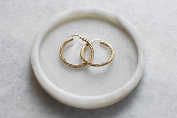 Overhead view of gold hoop earrings on a marble tray, top view of solid gold earrings on a marble jewelry holder