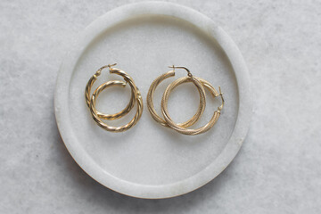 Overhead view of gold hoop earrings on a marble tray, top view of solid gold earrings on a marble jewelry holder