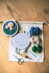 Flatlay of two embroidery hoops with funiched and unfinished projects, balls of yarn, scissors and...