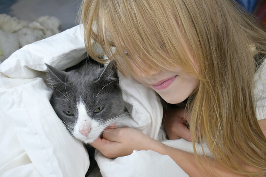 A little girl with brown hair strokes a gray cat while lying on the bed. The concept of love and care for one's neighbor.