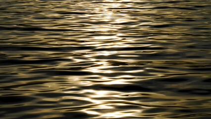 Sunlight plays on the calm sea waves. The surface of the sea water at sunset. Ripples on the water in close-up.
