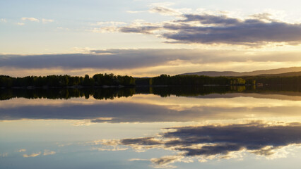 Sunset on the lake with a mirror image of the cloudy sky on the surface of the water. The concept of love for nature.