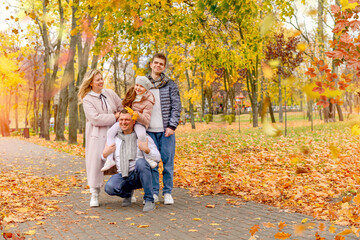 Fototapeta premium Banner with a Happy family in the autumn park: mom, dad, little daughter, teenage son. Background: yellow trees and foliage. Family vacation concept