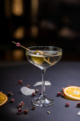 Martini cocktail decorated with an olive in a glass on a thin stem, on a table decorated with dried oranges