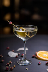 Martini cocktail decorated with an olive in a glass on a thin stem, on a table decorated with dried oranges