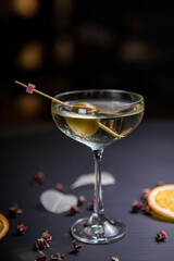 Martini cocktail decorated with an olive in a glass on a thin stem, on a table decorated with dried oranges