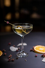 Martini cocktail decorated with an olive in a glass on a thin stem, on a table decorated with dried oranges