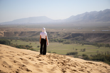 A girl on the sand in the mountains stands on a dune in Dagestan in the Caucasus