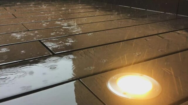V&iacute;deo de las gotas de lluvia golpeando el suelo. Gotas de lluvia rebotando en el suelo moderno de tablones de madera de un patio con paredes de ladrillo.