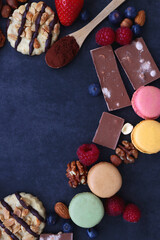 Macarons, chocolate, cookies, berries and various nuts on dark blue background. Top view.