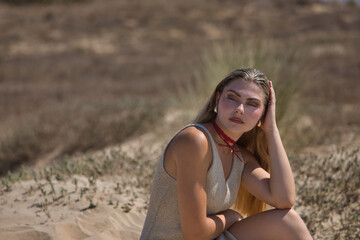 Young woman, beautiful, blue eyes, blonde, in shiny golden dress, sad, lonely and depressed, sitting on the sand. Concept beauty, fashion, trend, femininity.