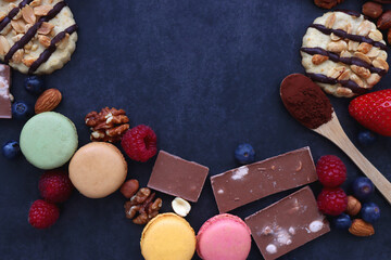 Macarons, chocolate, cookies, berries and various nuts on dark blue background. Top view.