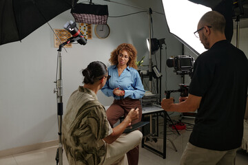 Director talking to model before shooting in studio while cameraman setting his camera