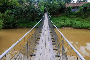 Obraz premium Suspension bridge over a muddy river in Kota Kinabalu, Malaysia, surrounded by lush greenery during the day