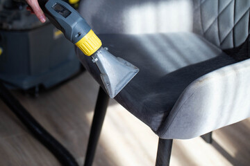 Dry cleaning gray soft chairs made of fabric upholstery with a washing vacuum cleaner. Cleaning company services, close-up