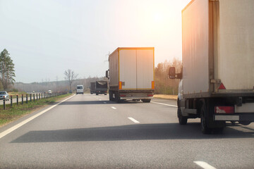 Traffic from trucks transporting goods along a country asphalt road against the backdrop of forest and sun in spring. Economics and business of cargo transportation. Copy space for text