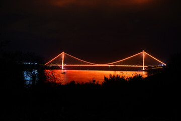Osmangazi Bridge. The photo of the bridge taken from the front while its colorful lights are on at night. The bridge lights are reflected on the sea, creating a magnificent view.