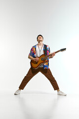 Powerful performance. Young man stands with wide stance, playing an electric guitar against white...
