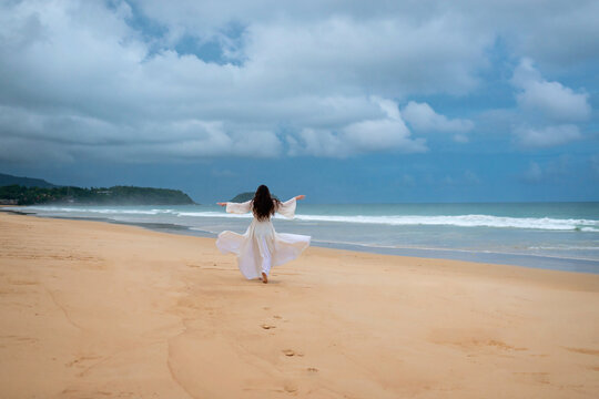 Back view young happiness asian traveller woman in white dress standing on beautiful sandy beach. Cute girl enjoy her tropical sea on relax holiday vacation during summer time