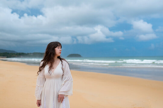 Portrait of young traveller woman in white dress and hat standing on beautiful sandy beach. Cute girl enjoy her tropical sea on relax holiday vacation during summer time and sunshine day